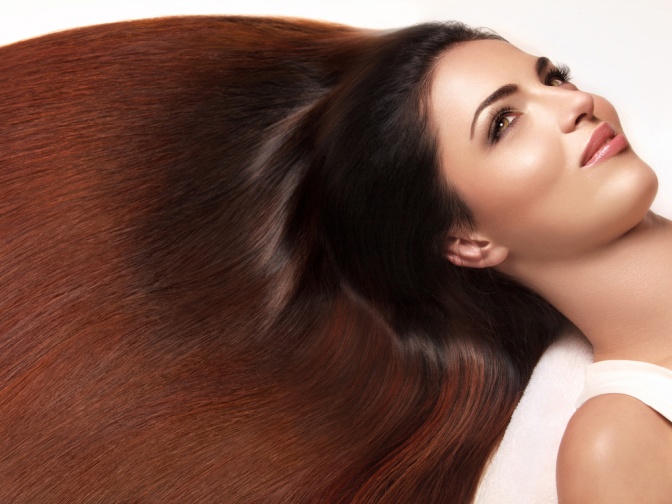 Die braunen langen Haare einer Frau sind ausgebreitet. Sie glänzen seidig und machen einen sehr gesunden Eindruck.
