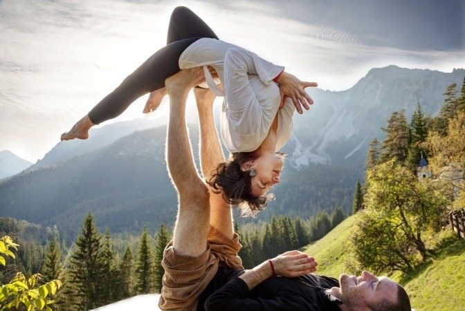 Ein Paar, welches im Freien auf einer Alm Yoga zusammen macht