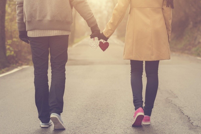 Ein Paar, das Hand in Hand mit jeweils einem Herz in der Hand einen Spaziergang macht