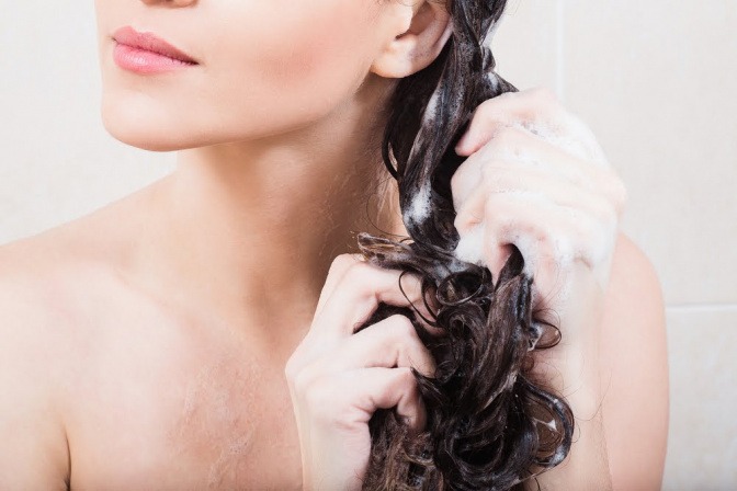Eine Frau mit langen dunklen Haaren wäscht sich gerade das Haar und schäumt es mit Shampoo auf