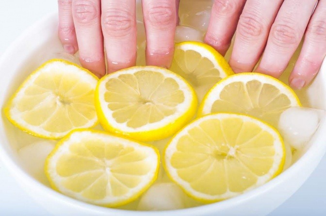 Eine Schüssel mit Wasser und Zitronenhälften befüllt, in der eine Hand ein Handbad macht