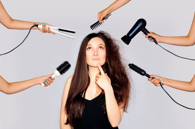 Eine Frau mit langen braunen Haaren umgeben von verschiedensten Stylingutensilien
