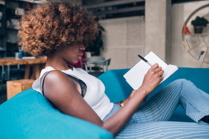 Eine junge Frau auf einer Couch schreibt in ihr Notizbuch