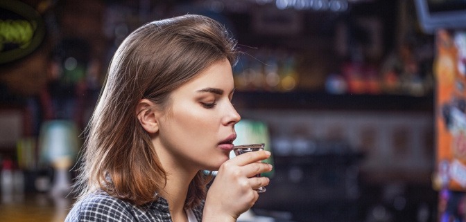 Frau mit unsicherem Blick hält Glas Alkohol vor dem Trinken