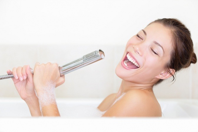 Eine Frau nutzt den Duschkopf als Mikrofon während sie badet und singt vor sich hin.