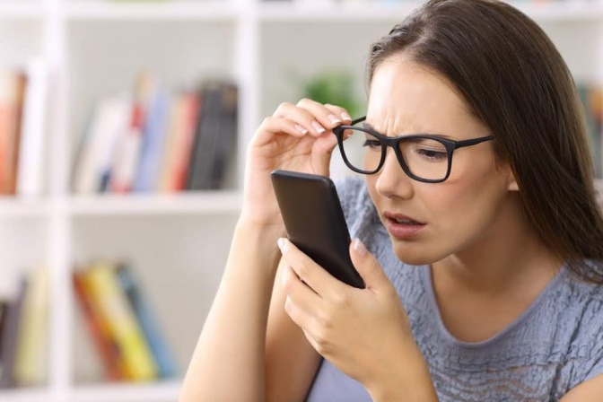 Eine Frau hält die Brille hoch, während sie auf ihr Smartphone sieht