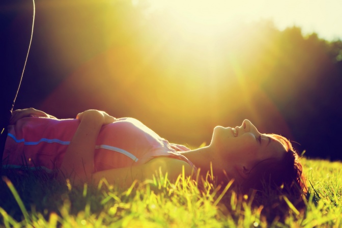Eine Frau liegt im Gras bei Sonnenschein