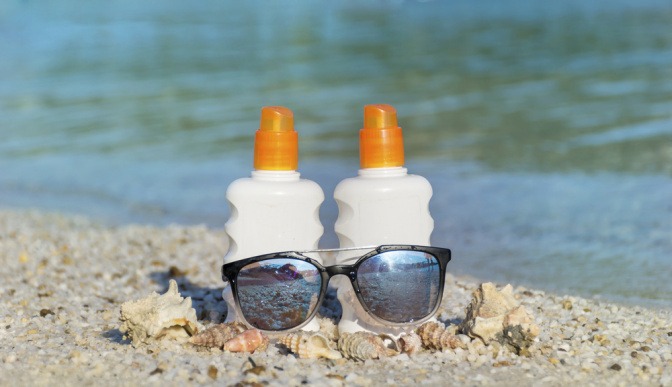 Zwei Flaschen Sonnenschutz und eine Sonnenbrille am Strand