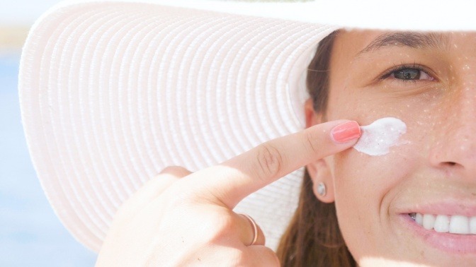 Eine Frau mit Sonnenhut trägt Sonnenschutz in ihrem Gesicht auf