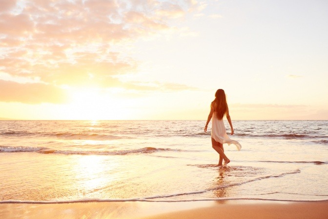 Eine Frau geht im Sonnenuntergang am Strand spazieren