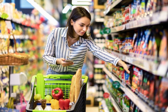 Eine junge Frau kauft im Supermarkt mit Einkaufsliste ein