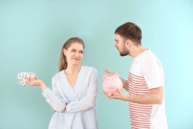 Junge Frau hält ein Bündel Geldscheine in der Hand, ihr Partner ein Sparschwein.