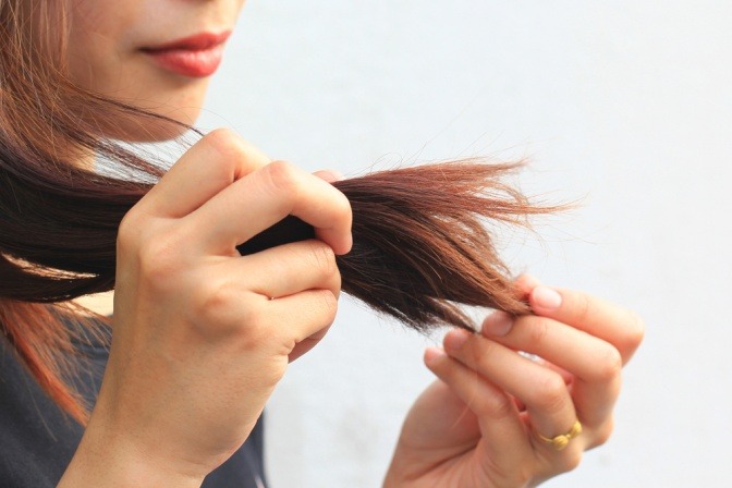 Eine Frau betrachtet Spliss in den Haaren