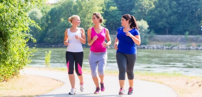 Drei Frauen betreiben Sport für Übergewichtige und laufen an einem sonnigen Tag gemeinsam durch einen Park.