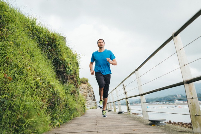Ein Mann joggt alleine an einer Kaimauer eines Flusses entlang.