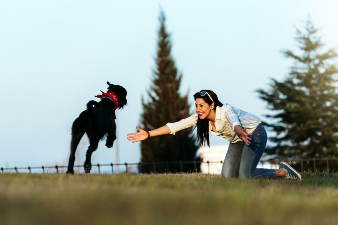 Hund rennt draußen auf sein Frauchen zu, sie empfängt ihn mit offenen Armen.