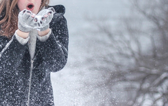 Eine Frau mit starkem Immunsystem bläst im Winter Schnee von den Händen
