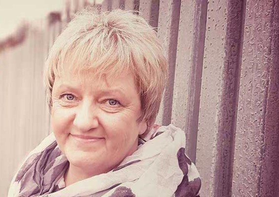 Stefanie Menzel steht vor einer Wellblechwand und lächelt in die Kamera