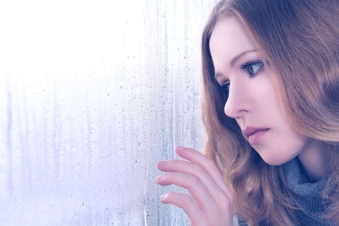 Eine Frau lehnt an einem von Regentropfen benetzten Fenster.