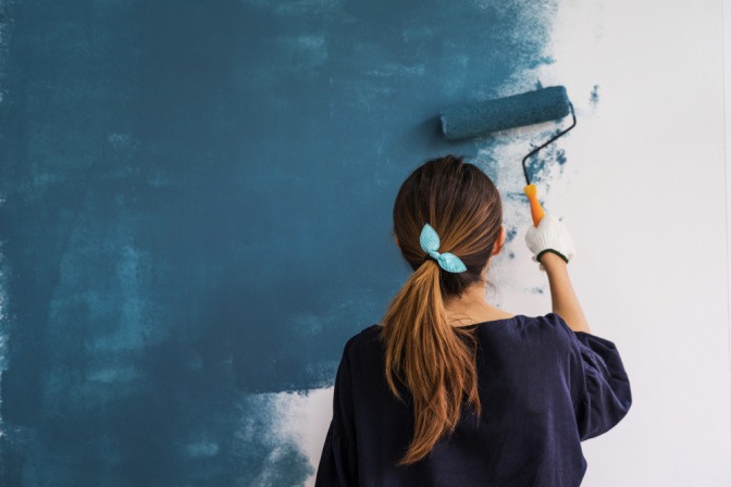 Eine Frau streicht eine Wand blau