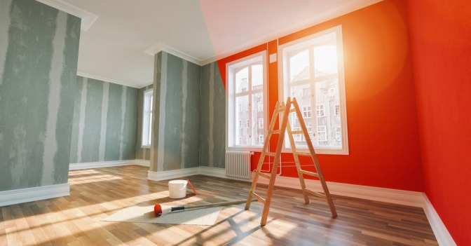 In einem Raum mit vorbereiteten Wänden stehen eine Leiter und Farbroller sowie Farbe