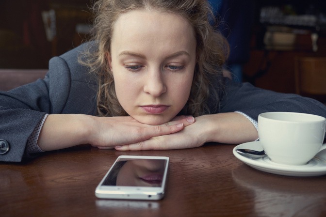 Traurige Frau sitzt in Cafe und starrt auf Ihr Smartphone.