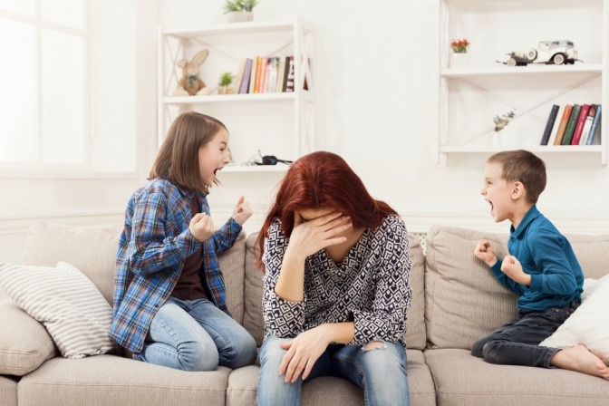 Frau zwischen zwei schreienden Kindern wirkt gestresst 