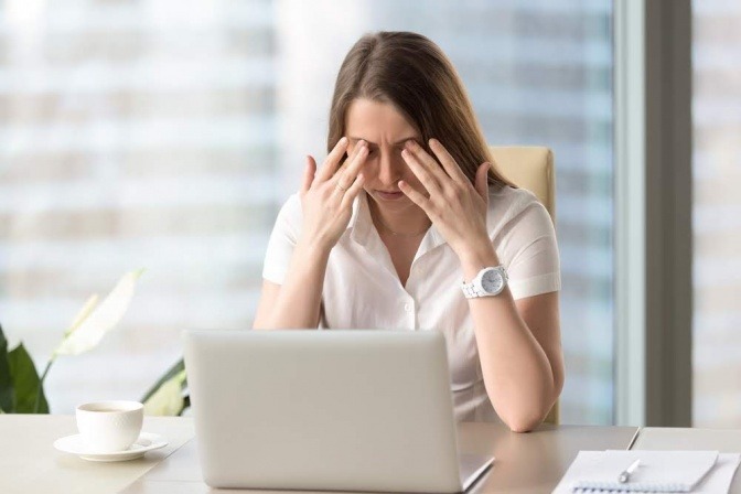 Frau vor PC hält gestresst die Augen zu
