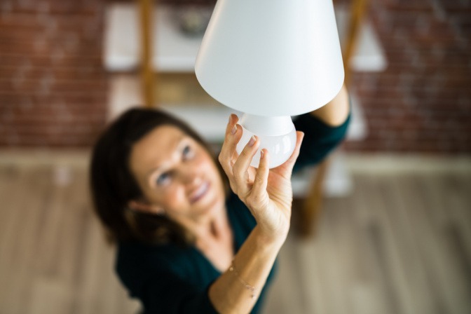 Frau schraubt energieeffiziente Glühbirne in eine Deckenlampe.
