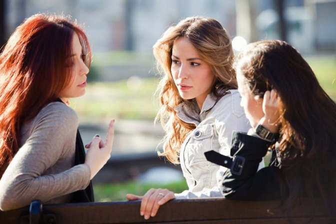 Drei Frauen sitzen draußen auf einer Bank und diskutieren über etwas.
