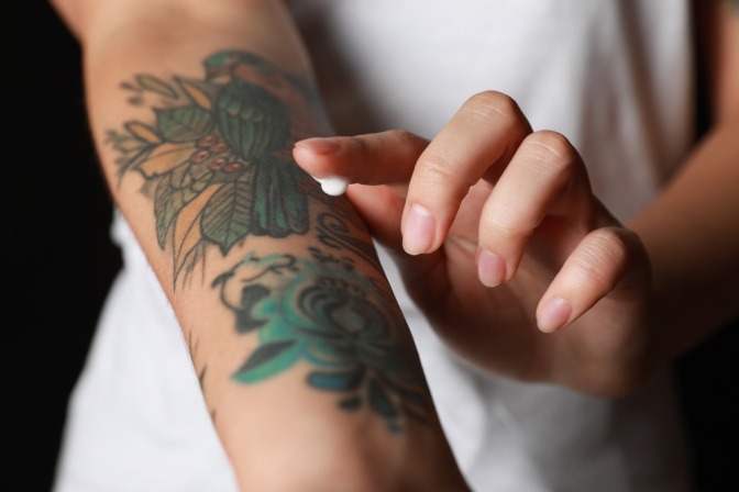 Frau cremt Haut mit Tattoo ein