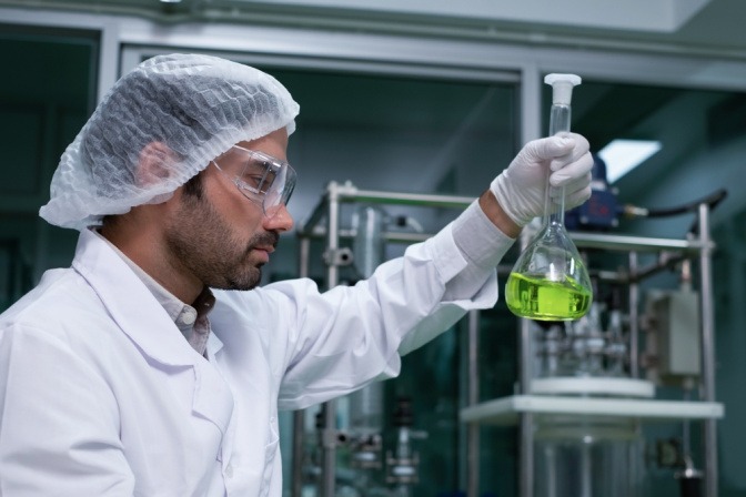 Chemiker im Labor hält Gefäß mit leuchtend grüner Flüssigkeit hoch.