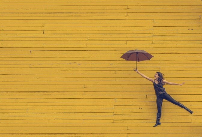 Eine Frau lässt sich von ihrem Regenschirm in die Luft heben und lächelt dabei. 