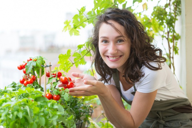 Frau mit Tomatenpflanze auf Balkon.