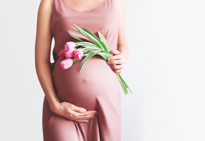 Schwangere mit Tulpenstrauß vor dem Bauch.