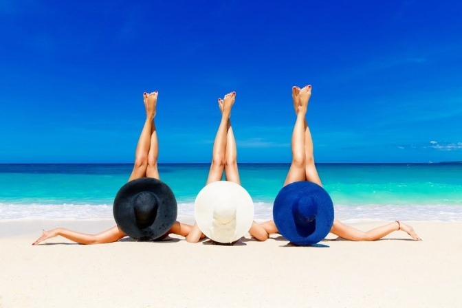 Drei Frauen liegen nebeneinander in der prallen Sonne am Strand. 