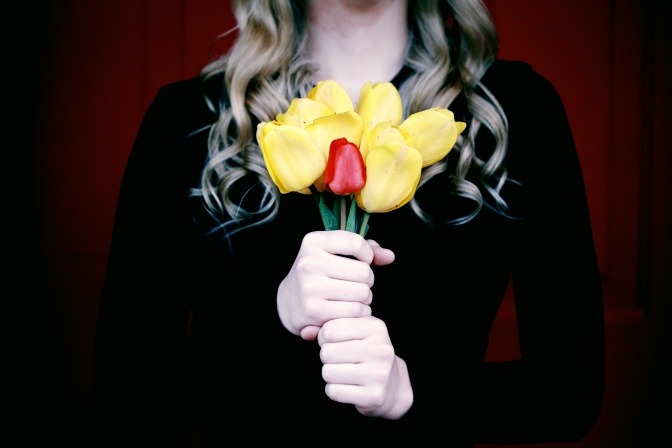 Eine Frau umklammert einen Blumenstrauß, der aus sechs großen gelben Rosen und einer kleinen roten Rose besteht.