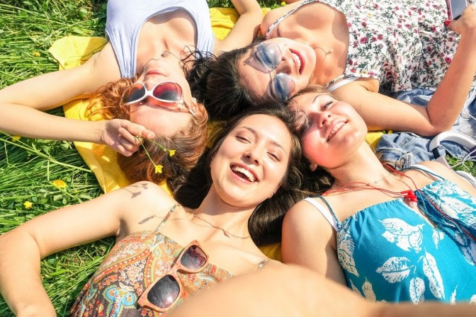 Vier Freundinnen liegen an einem sonnigen Tag auf einer Wiese. 