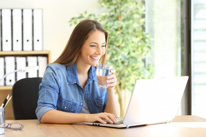 Frau mit Wasserglas vor Computer gegen Müdigkeit