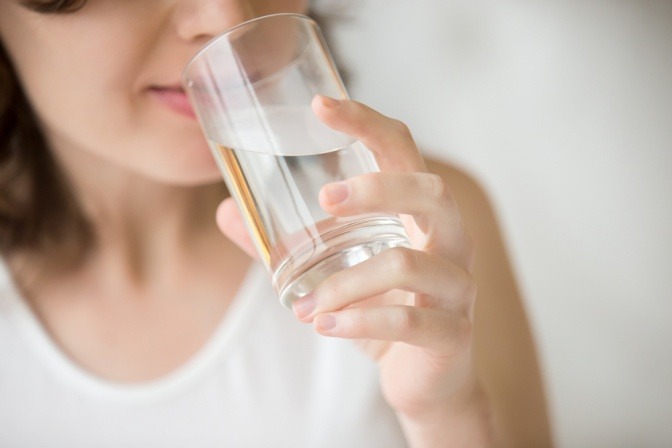 Frau trinkt aus Wasserglas gegen schwere Beine