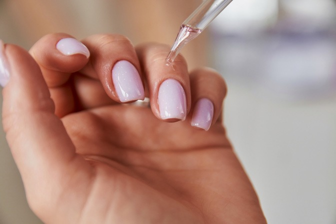 Eine Frau gibt Nagelöl auf ihre Fingernägel