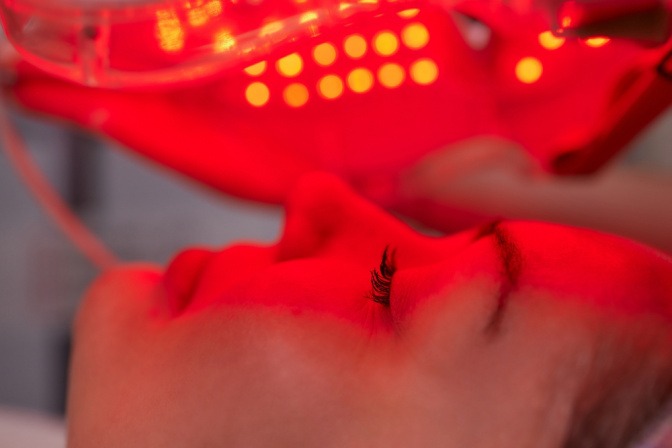 Eine Frau nutzt eine Lichttherapie-Maske mit rotem Licht