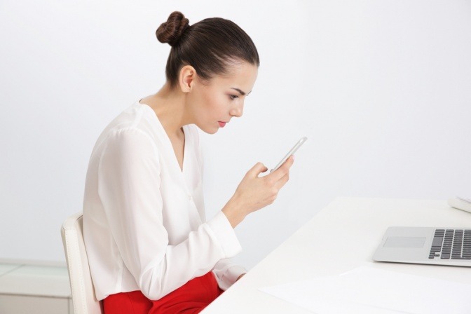 Frau am Schreibtisch vor Smartphone und Computer.