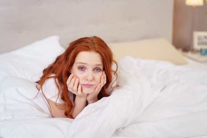 Unruhiger Schlaf ist für die Frau in diesem Bild wohl ein vertrautes Problem. Sie liegt bäuchlings im Bett, die Arme sind angewinkelt, ihr Kopf liegt auf den Händen. Sie wirkt erschöpft, resigniert und genervt.