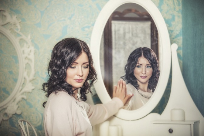 Frau vor dem Spiegel wird von ihrem Spiegelbild betrachtet