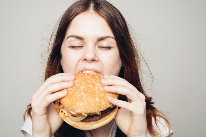 Frau mit Burger als Ursache für Müdigkeit nach dem Essen