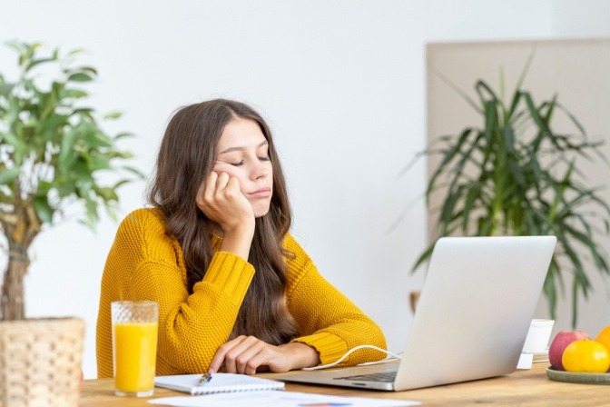 Junge Frau sitzt gelangweilt und teilnahmslos vor ihrem Laptop.