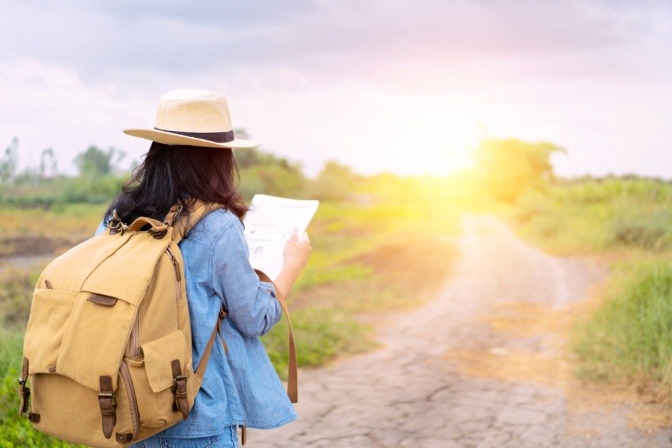Weibliche Touristin benutzt eine Karte, um die Richtung eines Ortes zu finden. Vor ihr strahlt die Sonne verheißungsvoll.