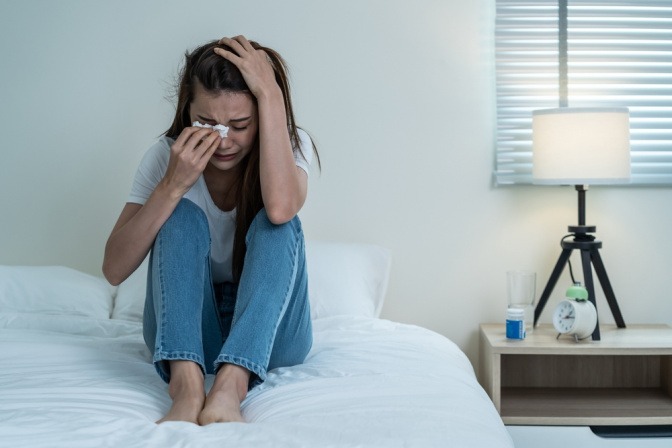 Weinende Frau sitzt auf ihrem Bett.