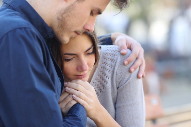 Ein junger Mann nimmt eine junge Frau tröstend in den Arm